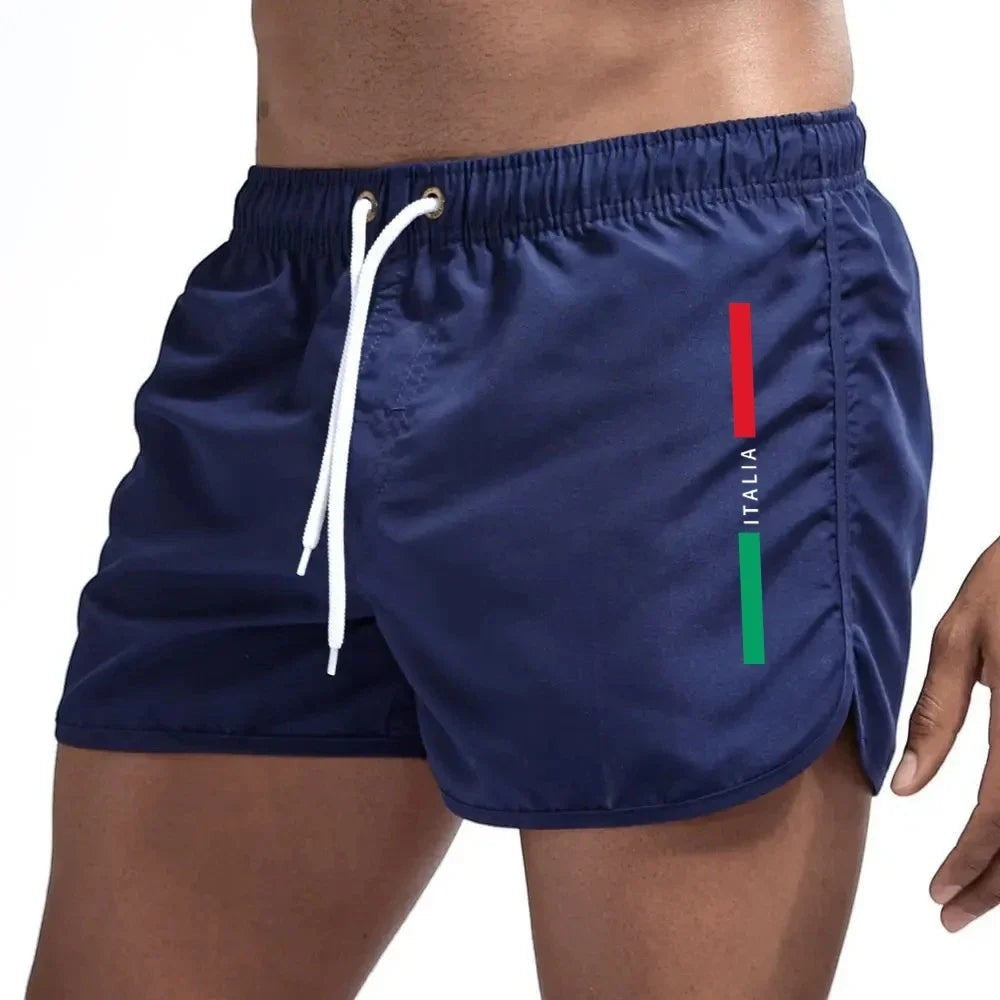 Bañadores cortos azul marino de Variedad Online para hombre, con cordón blanco, cintura elástica y detalle de la bandera italiana en el lateral.
