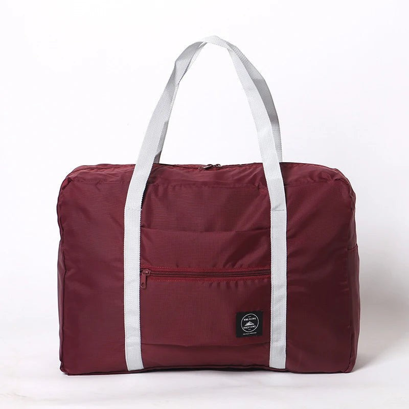 Bolsa de viaje plegable Variedad Online de nailon impermeable color burdeos con asas grises y bolsillo frontal con cremallera.