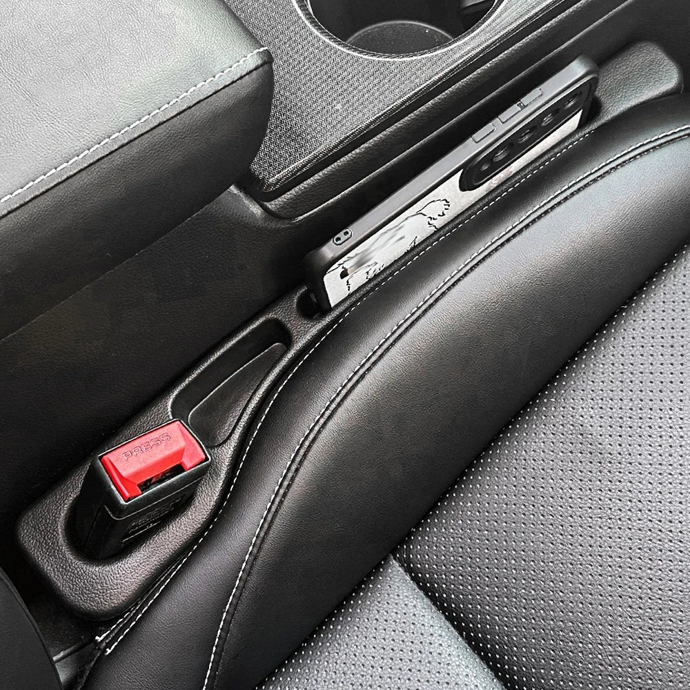 Organizador de huecos para asientos de coche Variedad Online en cuero negro con costuras blancas, con teléfono y hebilla de cinturón de seguridad.